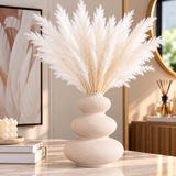Beige textured ceramic vase with white dried pampas grass on a wooden console table.