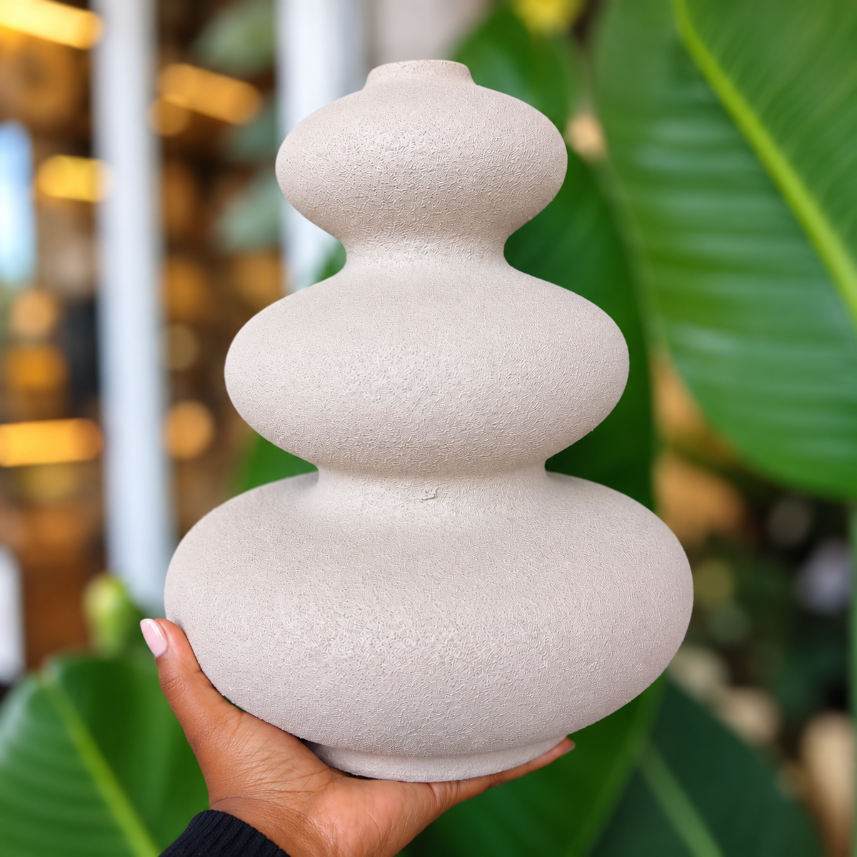 Minimalist beige stone-look ceramic vase with a three-tier design, held in hand.
